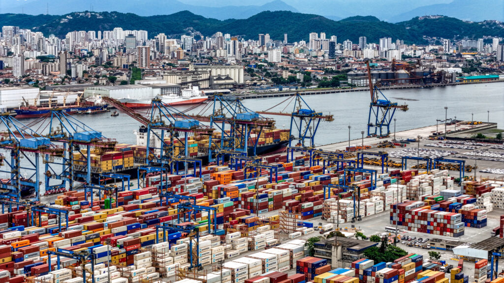 Vista aérea do terminal de contêineres no Porto de Santos com movimentação logística e navios cargueiros.
