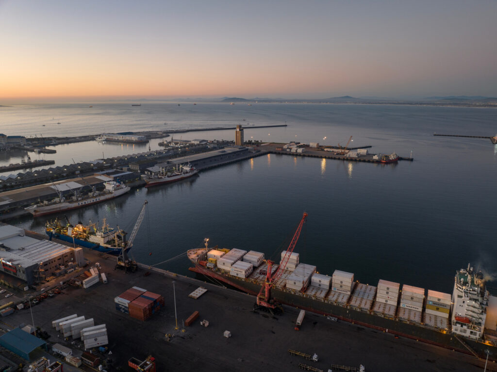 Operação logística em terminal portuário com navios cargueiros e contêineres em área de embarque.