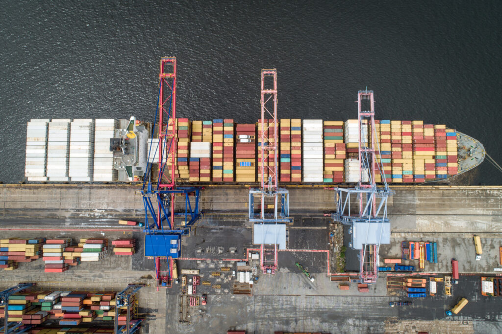 Vista aérea de porto com movimentação de containers e controle de acesso no gate portuário.