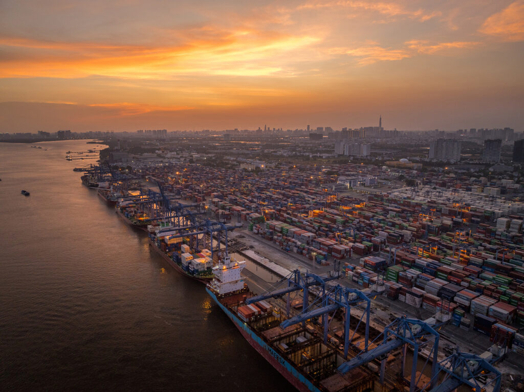 Porto com grande movimentação de containers ao entardecer representando fluxo logístico contínuo.
